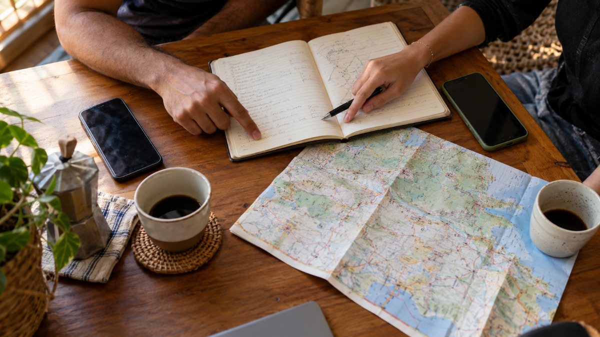 Mãos apontando para caderno com anotações de planejamento de viagem sobre mesa de madeira